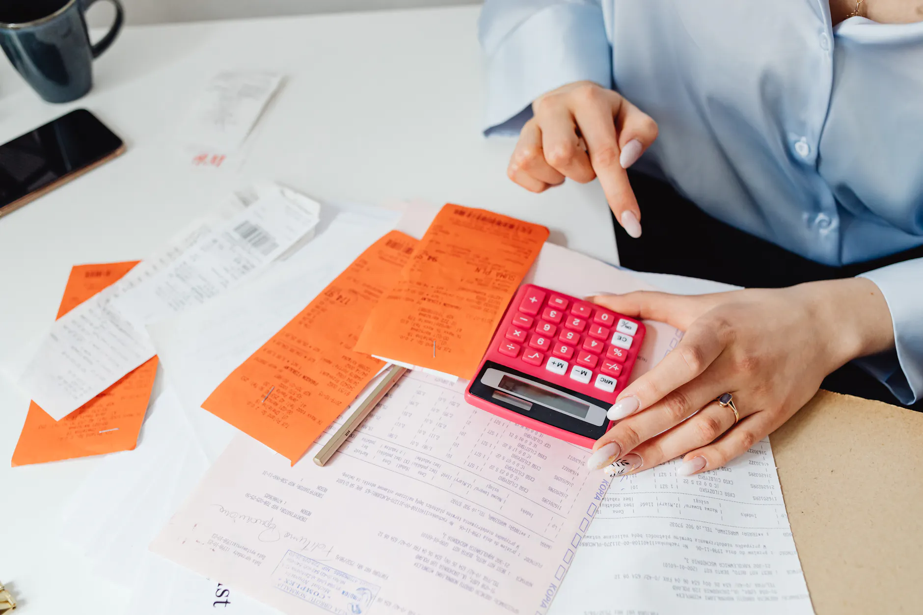 Person calculating program costs at a desk with receipts, a calculator, and paperwork.