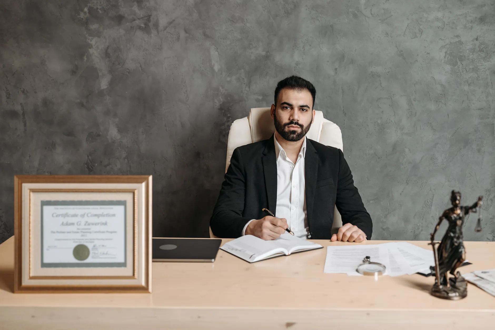 Confident man sitting at a desk surrounded by legal documents and a certificate.